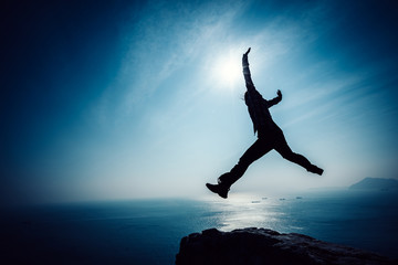 hiker jumping on sunrise seaside cliff edge