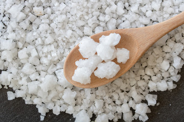 White salt in wooden spoon with black background.