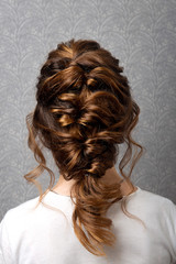 Obraz premium Hairstyle Greek braid on the head of a brown-haired woman back view close-up on a gray background.