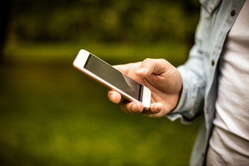 Young man in park using mobile phone. Focus is on hand. Close up.