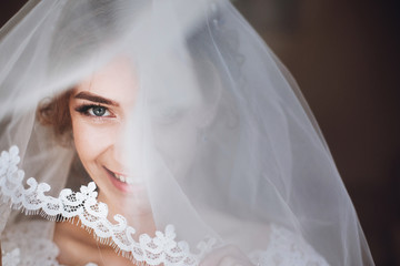 happy stylish bride smiling and looking under veil. space for text. gorgeous emotional bride getting ready and having fun in the morning
