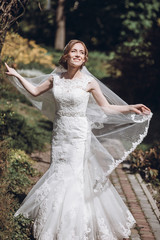 Fototapeta na wymiar Happy newlywed bride swirling in white wedding dress in romantic garden with floral archway
