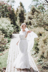 Fototapeta na wymiar beautiful gorgeous bride with veil posing and having fun in sunny spring park. happy woman standing in green garden. happy marriage moments. elopement concept