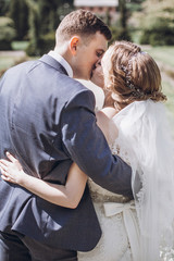 beautiful gorgeous bride and groom kissing in sunny spring park and enjoying day. happy wedding couple relaxing in green garden. happy marriage moments. elopement concept