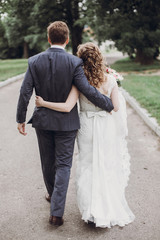 Fototapeta premium beautiful gorgeous bride and groom walking in sunny park and embracing. happy wedding couple hugging in green garden. happy romantic moments. elopement concept.