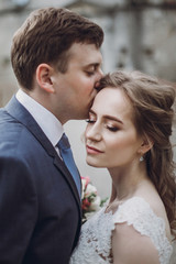 Sensual groom kissing beautiful bride on the forehead, newlywed couple portrait, beautiful married couple posing outdoors