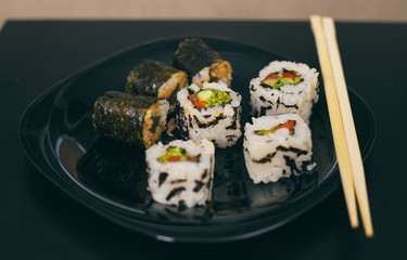 Delicious and healthy vegan rolls lie in a black plate on the table.