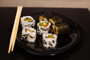 Delicious and healthy vegan rolls lie in a black plate on the table.
