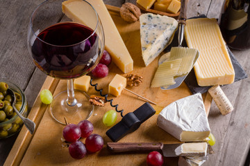Palette of many types of cheese and some grapes, olives and wine.