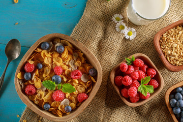 Cornflakes and other cereals with fresh fruits of raspberries, blueberries and milk on healthy breakfast. Above view.
