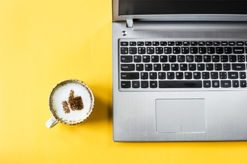 A cup of cappuccino on which is drawn a smile like a thumb up. Next to the laptop. Communication in...