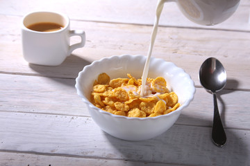 Milk pouring into a bowl of delicious corn flake cereals and cap with espresso coffee. Morning breakfast.