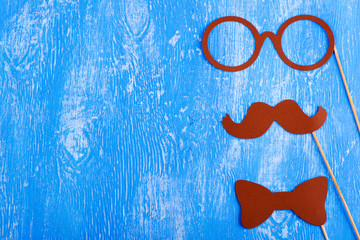 Paper glasses, a mustache and a bow tie on a blue wooden background.