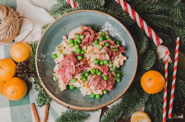 Top view russian traditional salad Olivier with vegetables and meat. Salad on a plate on a on wooden board, orange mandarin, candy sticks, christmas tree background. New year food theme.