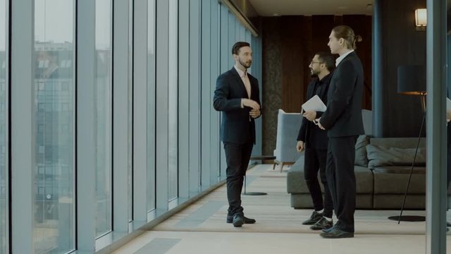 Three businessmen in business suits standing in front of big panoramic window with city view and talking. 4K