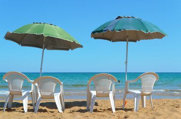 Chairs with parasols on the beach in front of the blue Sea 