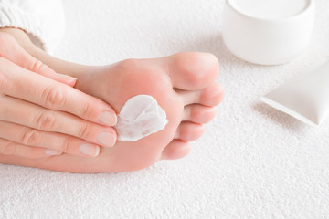 Groomed woman's hands applying feet moisturizing cream. Barefoot on the white towel. Cares about clean and soft legs skin. Healthcare concept.
