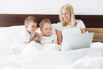 Young woman with her two kids using digital tablet in bed at home.