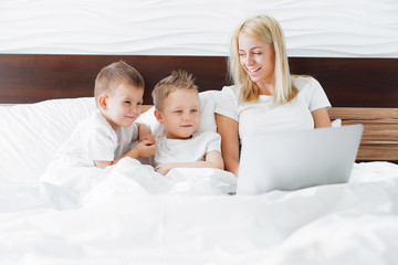 Fototapeta premium Young woman with her two kids using digital tablet in bed at home.