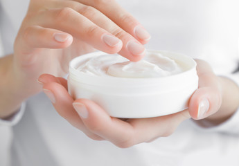 Beautiful groomed woman using moisturizing cream for clean and soft skin. Cream jar in hands. Healthcare concept.
