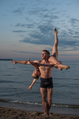 Fototapeta na wymiar Young guy and girl perform beautiful dance elements on the beach on the sand in bathing suits. Holding hands, performs support. Ballet.
