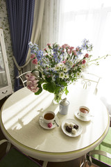 Sunny living room with a big bouquet on the round table, interior in Provence style