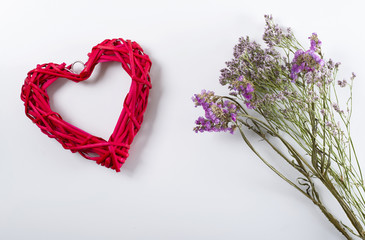 Close up of lilac flowers next to red heart on white background. Isolated. Copyspace