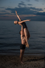 Young guy and girl perform beautiful dance elements on the beach on the sand in bathing suits. Holding hands, performs support. Ballet.