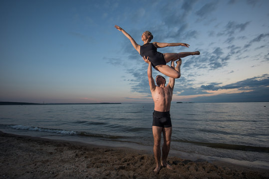 Young guy and girl perform beautiful dance elements on the beach on the sand in bathing suits. Holding hands, performs support. Ballet.