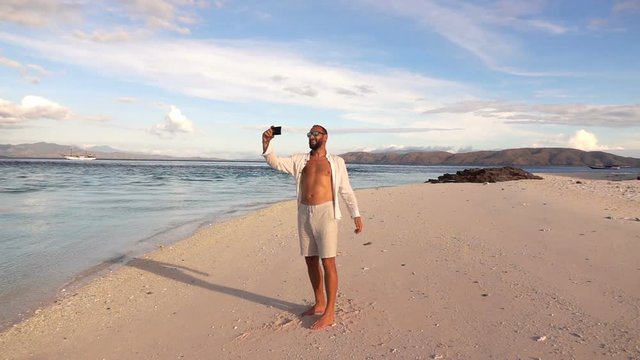 Happy man taking selfie photo with cellphone on beach, super slow motion
