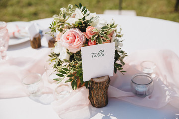 Banquet wedding table stands in the backyard, on the table are plates, glasses, candles and compositions of flowers and greenery