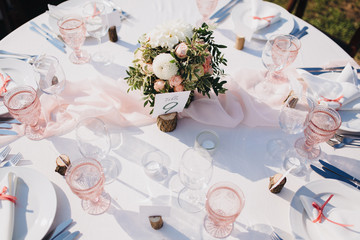 Banquet wedding table stands in the backyard, on the table are plates, glasses, candles and compositions of flowers and greenery