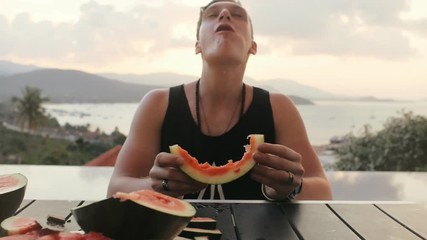 Funny man eating watermelon at speed on evening dinner. Cheerful man competing in fast eating watermelon on summer balcony