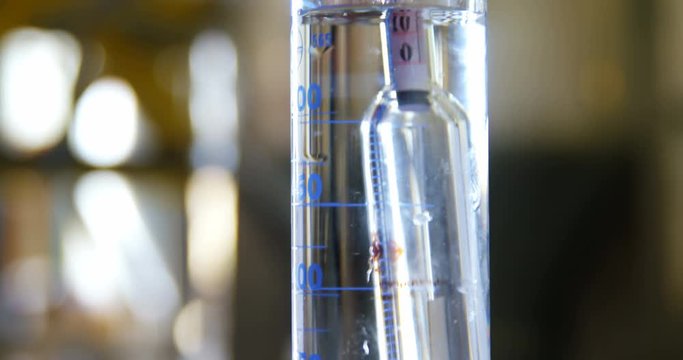 Male worker examining gin in measuring cylinder 
