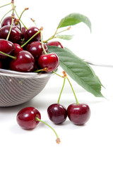 Steel colander with red sweet cherry isolated on a white background..