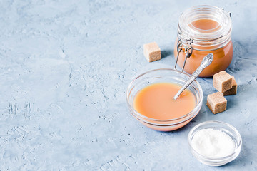 Homemade salted caramel sauce in glass jar on light blue concrete background. Selective focus, space for text.