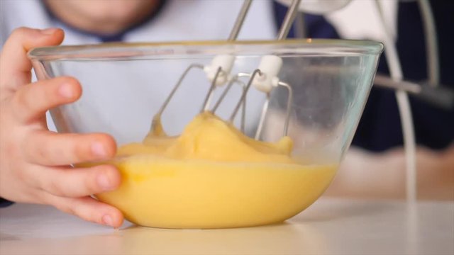 Mother and son are cooking an omelette; they are whisking eggs together with a handheld egg-beater; close-up on the glass bowl and eggs