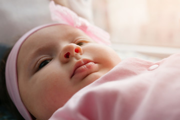A little baby girl lies on a bed in pink clothes and a bandage on her head