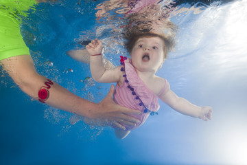 Obraz na płótnie Canvas Mom teaches little girl with an open mouth swimming underwater in the pool