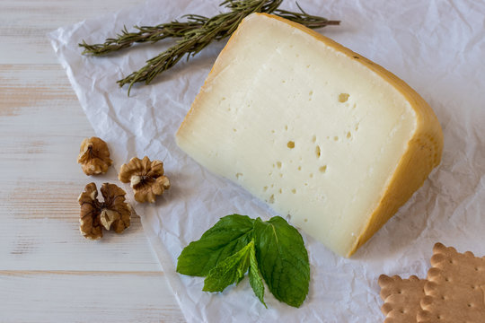 Greek cheese graviera on white wooden board with nuts and herbs.