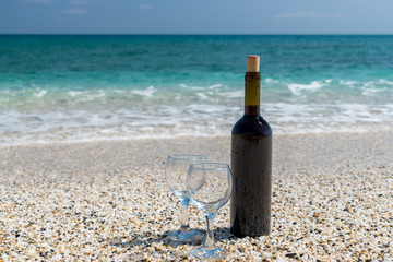 Bottle of red wine with wine glasses on the beach at the summer sunny day. Sea on the background.