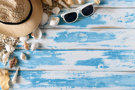 Seashells on blue wooden board with straw hat and sunglasses. Summer holiday background.