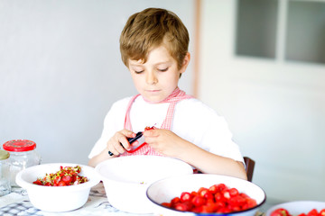 Little blond kid boy helping and making strawberry jam in summer