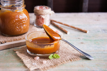 Homemade salted caramel in jar on wooden background