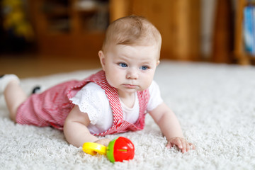Fototapeta na wymiar Cute baby playing with colorful rattle education toy. Lttle girl looking at the camera and crawling