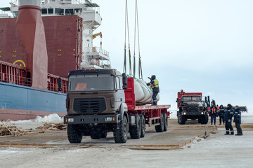 Unloading the ship in the frozen sea. A truck standing on the ice. On the ice laid wooden decks so he not failed.