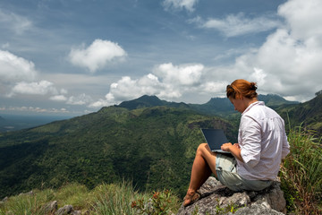 Caucasian girl working on her computer on the top of the mountain. Concept or remote work in internet for frilancer
