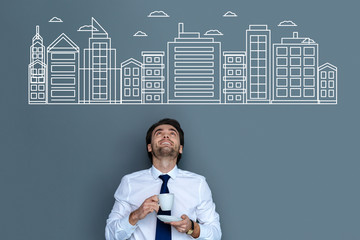 Big city. Emotional cheerful engineer smiling and dreaming about moving to a big city while drinking coffee © zinkevych