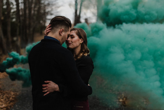Young couple kissing in forest by green smoke cloud