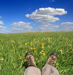 Legs of traveler sitting on green spring meadow